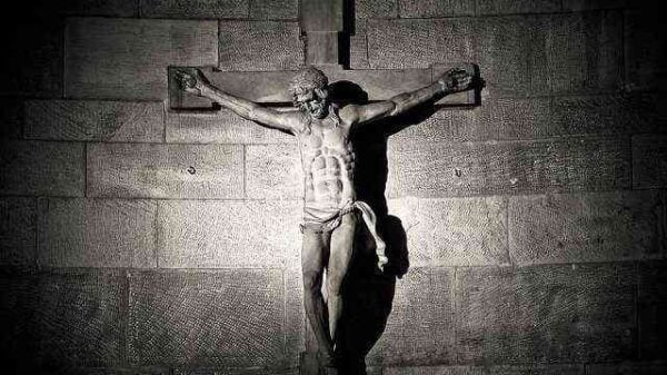 An einer grauen dunklen Mauerwand hängt ein Kruzifix: Jesus Christus hängt am Kreuz in erschütternder Weise