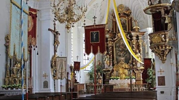 Das Kirchenjahr in seinen Festen: die Kirche ist geschmückt nicht nur mit dem barocken Hochaltar, Seitenaltar, Kanzel und Statuen, sondern auch mit einem weiß-gelben, von der Decke zu beiden Seiten hin herab fallenden Band und zweier Prozessionsfahnen im Vordergrund