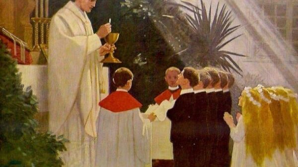 Der Priester steht, den Kelch und die konsekrierte Hostie über dem Kelch in seinen Händen vor den Kindern
